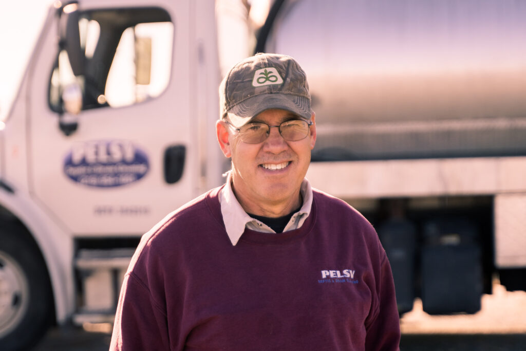 man smiling with pelsy septic truck in background